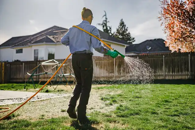 Colonial technician fan-spraying a backyard lawn under an autumn tree