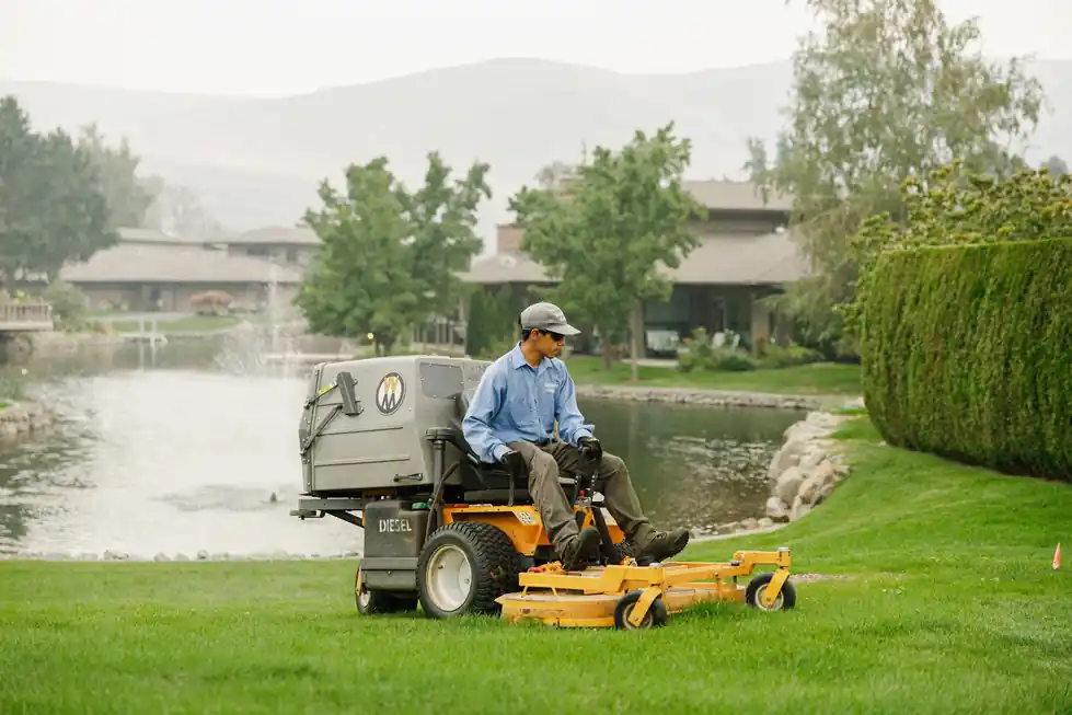 Colonial maintenance technician on a stand-on mower beside a pond